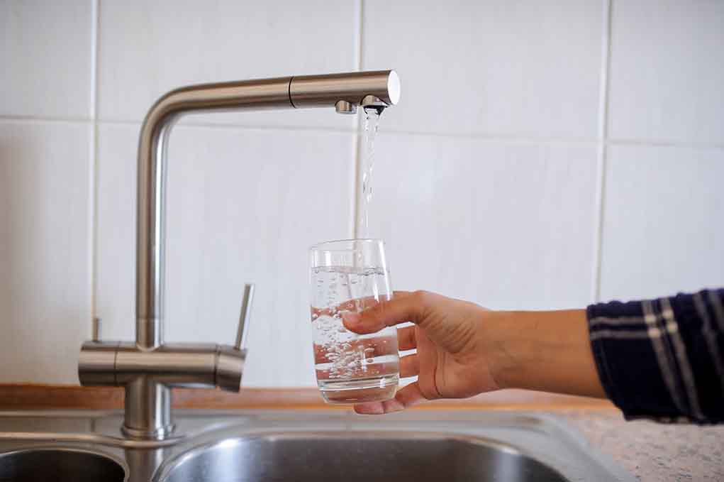How Does Fluoride Exposure Affect Young Minds and Brain Health? Hand filling glass with water from faucet.
