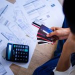 Person holding credit cards amidst bills and calculator