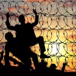 Silhouettes and barbed wire against sunset sky backdrop