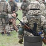 Soldiers in camouflage gear gathered on grass field.