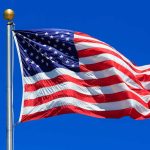 American flag waving against a clear blue sky.