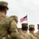 Soldiers standing with American flag in background sky