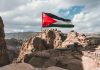 Flag flying over rocky, mountainous landscape with tents.