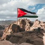 Flag flying over rocky, mountainous landscape with tents.
