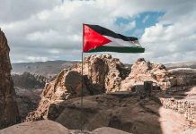 Flag flying over rocky, mountainous landscape with tents.