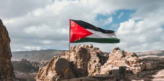 Flag flying over rocky, mountainous landscape with tents.