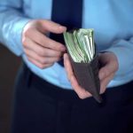Person holding wallet filled with cash in hands
