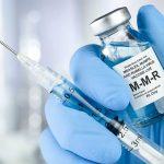 Syringe and MMR vaccine vial in gloved hand