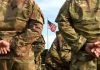 Soldiers in uniform standing with American flag visible