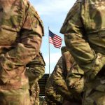 Soldiers in uniform standing with American flag visible