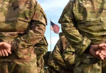Soldiers in uniform standing with American flag visible