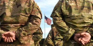 Soldiers in uniform standing with American flag visible