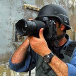Person in helmet taking photos with a large camera.