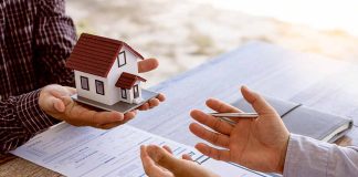 Hands exchanging miniature house over contracts
