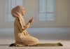 Woman praying indoors on a prayer mat.