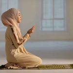 Woman praying indoors on a prayer mat.