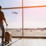 Traveler with luggage watches airplane take off at airport.