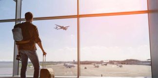 Traveler with luggage watches airplane take off at airport.
