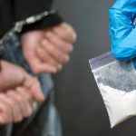 Person handcuffed police holding bag of white substance
