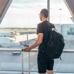 Person with backpack at airport window watching airplanes