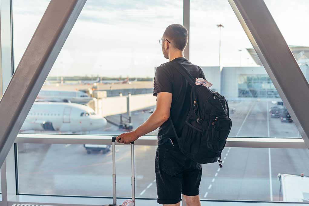 Person with backpack at airport window watching airplanes