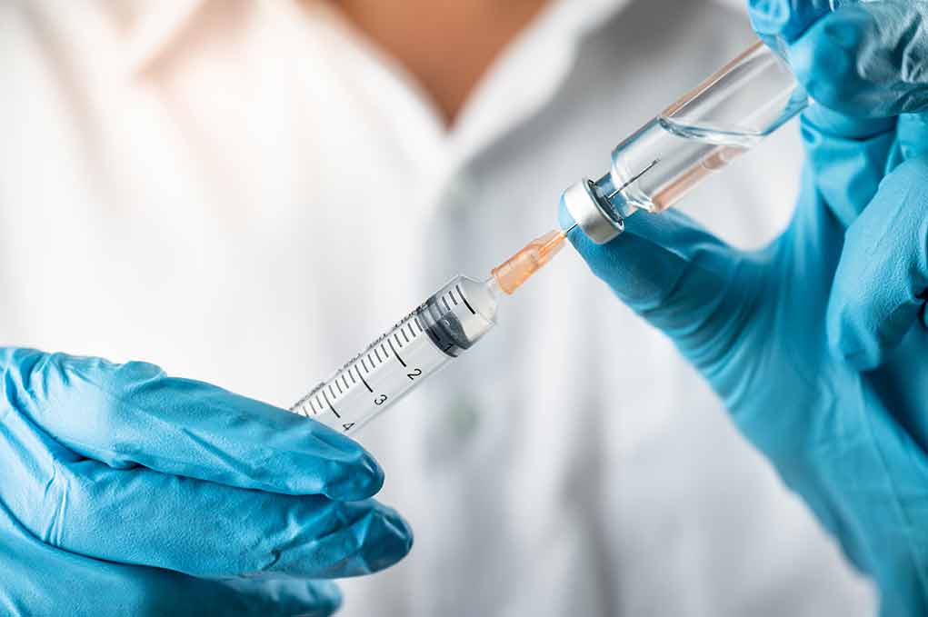 Gloved hands preparing syringe from vial