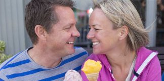 Couple smiling with ice cream cones outside bench