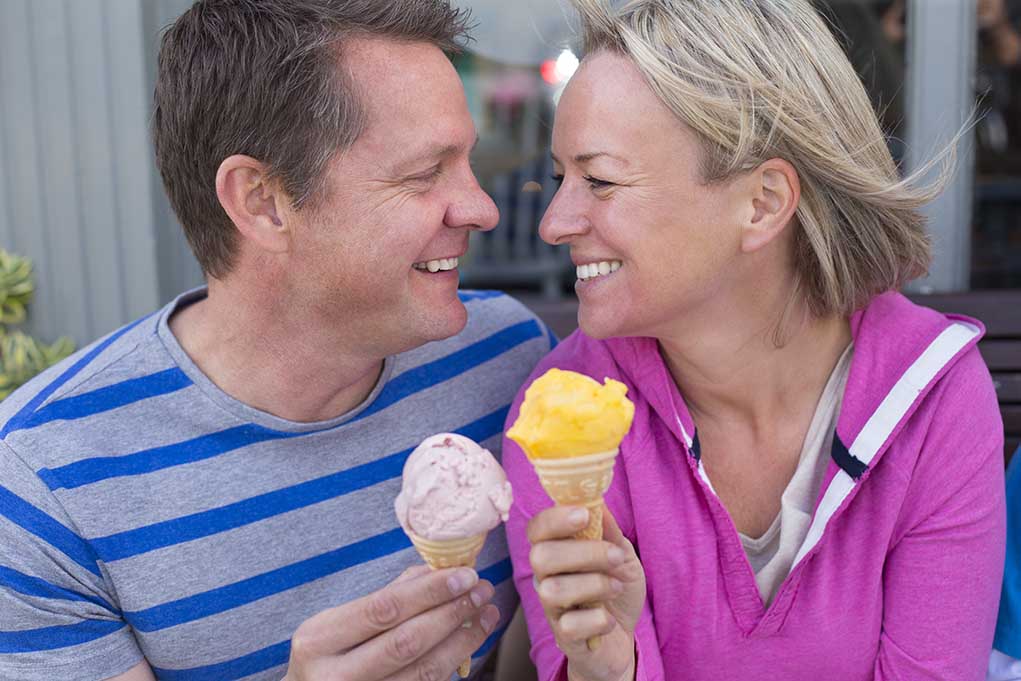 Couple smiling with ice cream cones outside bench