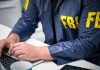 Person in FBI jacket typing on a laptop