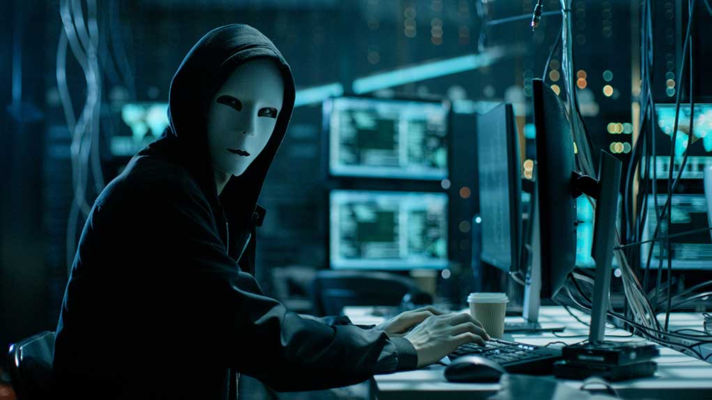 680078920 featured image Person wearing mask and hoodie at computer desk