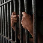 Hands gripping prison cell bars tightly