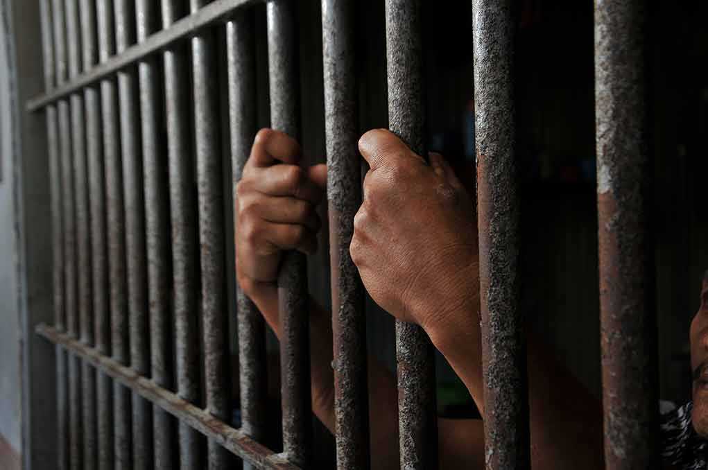 Hands gripping prison cell bars tightly