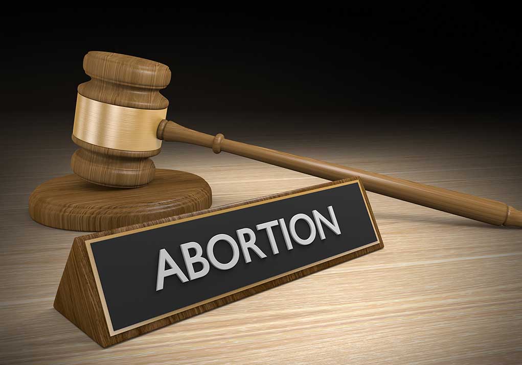 Gavel and sign reading Abortion on a wooden surface