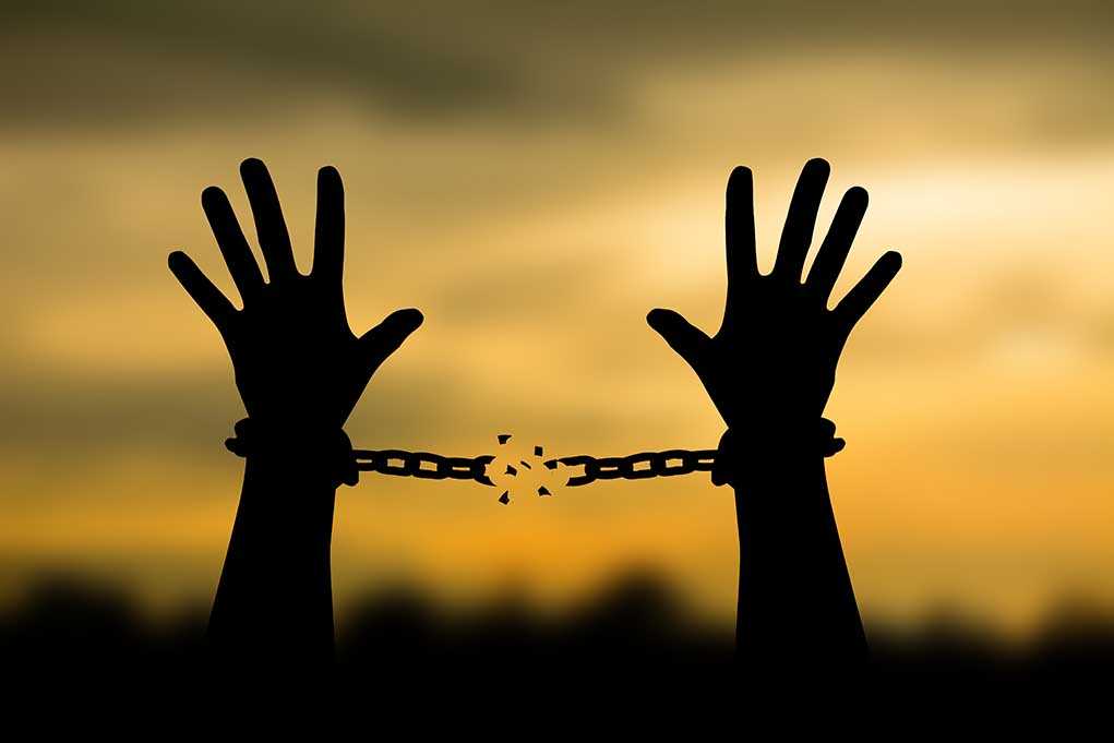 Hands breaking free from chains at sunset