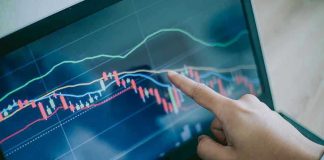 Hand pointing at stock market graph on laptop screen