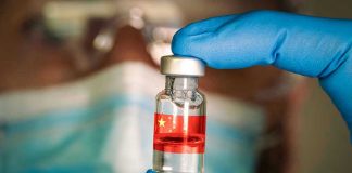 Gloved hand holding vial with red liquid and flag