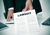 Person holding a document titled LAWSUIT in office