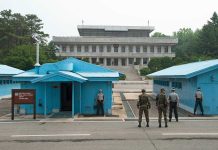 Military personnel standing near blue buildings at a border crossing