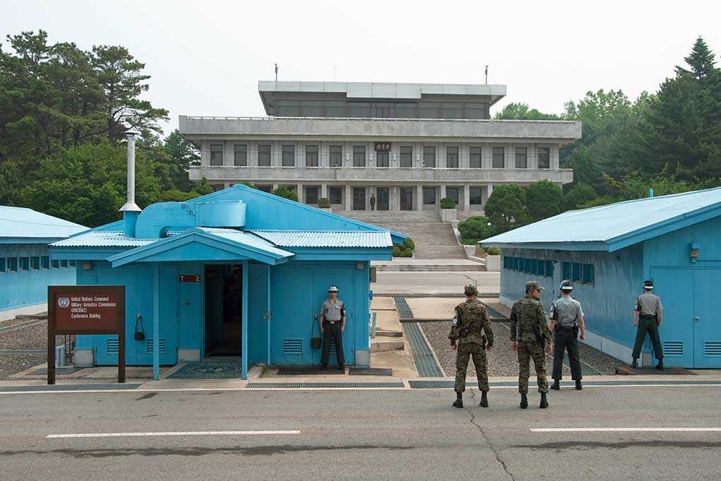Military personnel standing near blue buildings at a border crossing