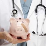 A doctor in a white coat holding a piggy bank with a bandage on it