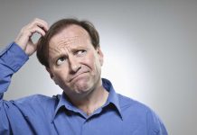 A man in a blue shirt with a confused expression, scratching his head