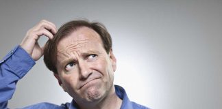A man in a blue shirt with a confused expression, scratching his head