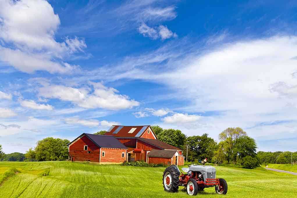 A vintage tractor in front of a red barn on a sunny day