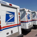 Row of USPS mail trucks parked in lot.
