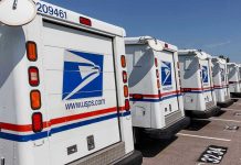 Row of USPS mail trucks parked in lot.