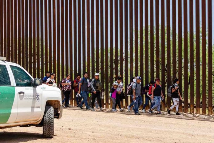People walking beside tall fence and border patrol vehicle
