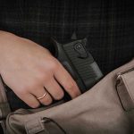 Hand placing handgun into beige handbag