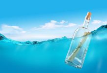 A glass bottle with a rolled-up message floating in clear blue water under a bright sky