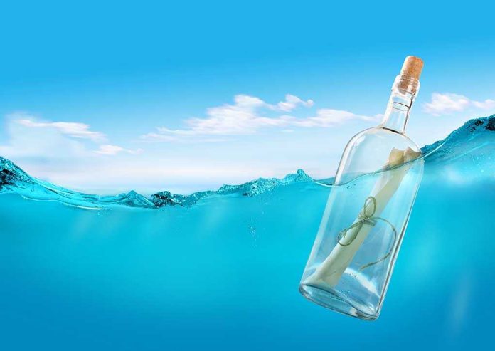 shutterstock_105691901.jpg A glass bottle with a rolled-up message floating in clear blue water under a bright sky