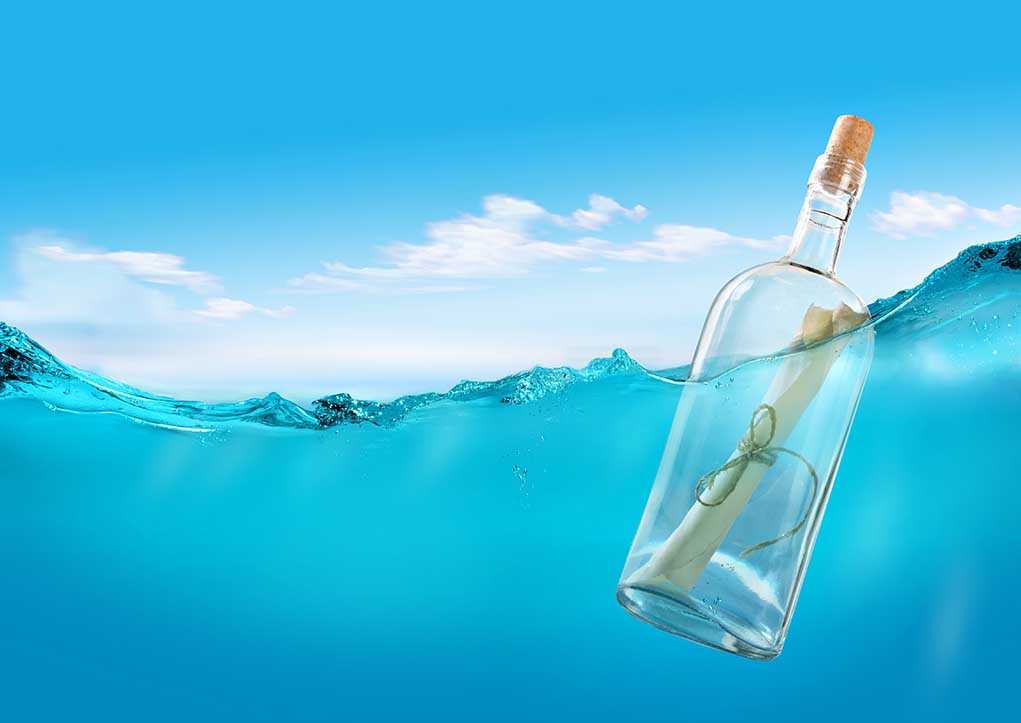 A glass bottle with a rolled-up message floating in clear blue water under a bright sky